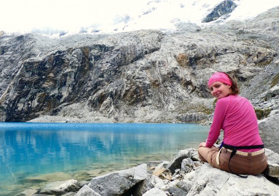 Anna sitting on the shore of a turquoise lake, with a mountain in the background